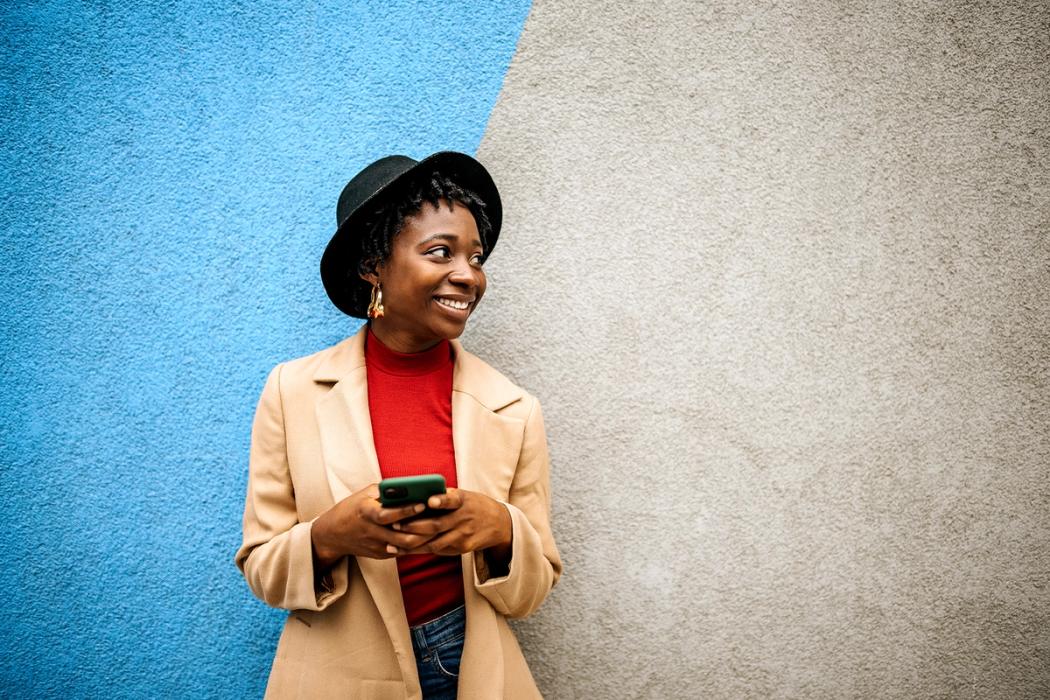 A social media manager smiles as she works on a post on her phone.