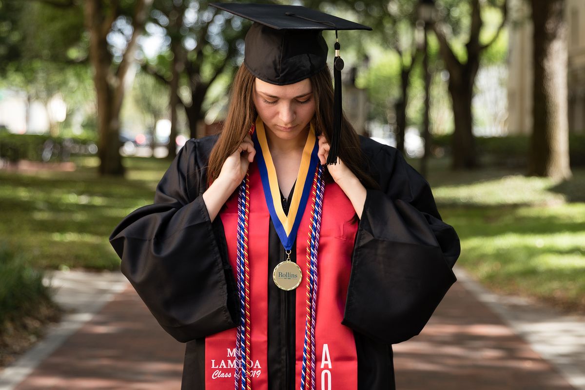 A college graduate poses in her cap and gown on the Rollins College campus.