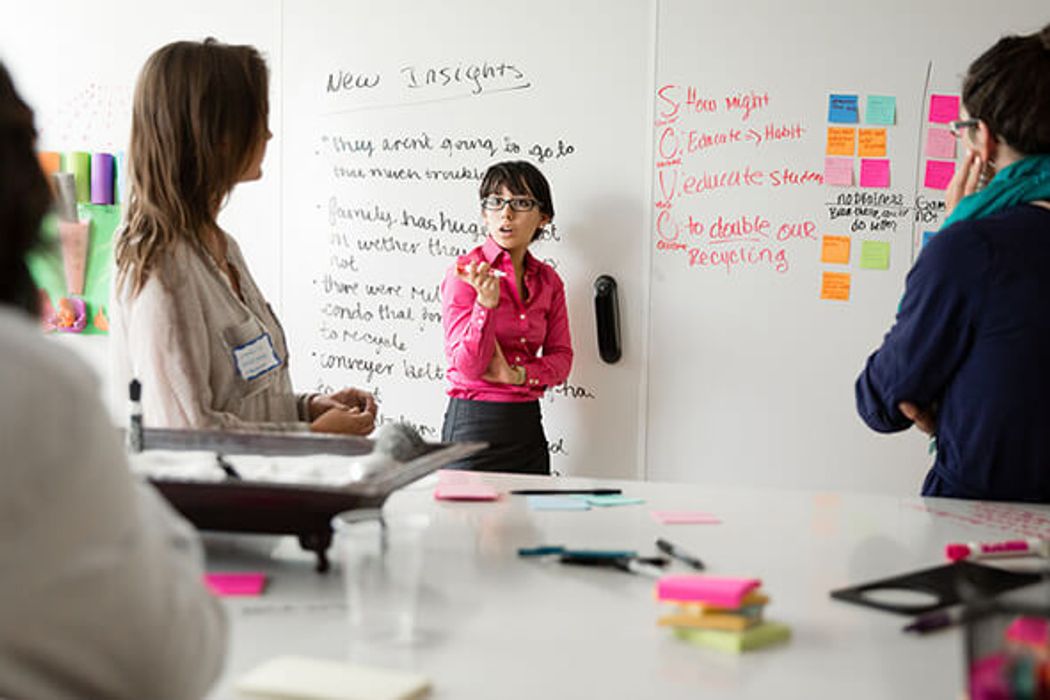 Students brainstorming at a whiteboard covered in notes during a design thinking exercise.