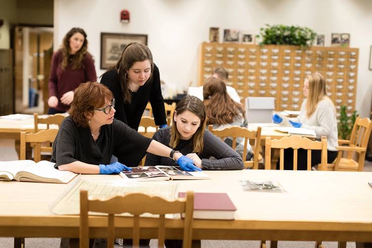 A professor works with a pair of students in the Rollins College archives.