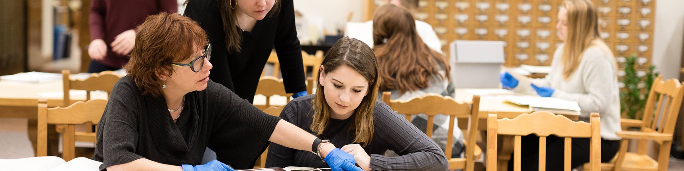 Rollins college students work with a faculty member in the library archives.