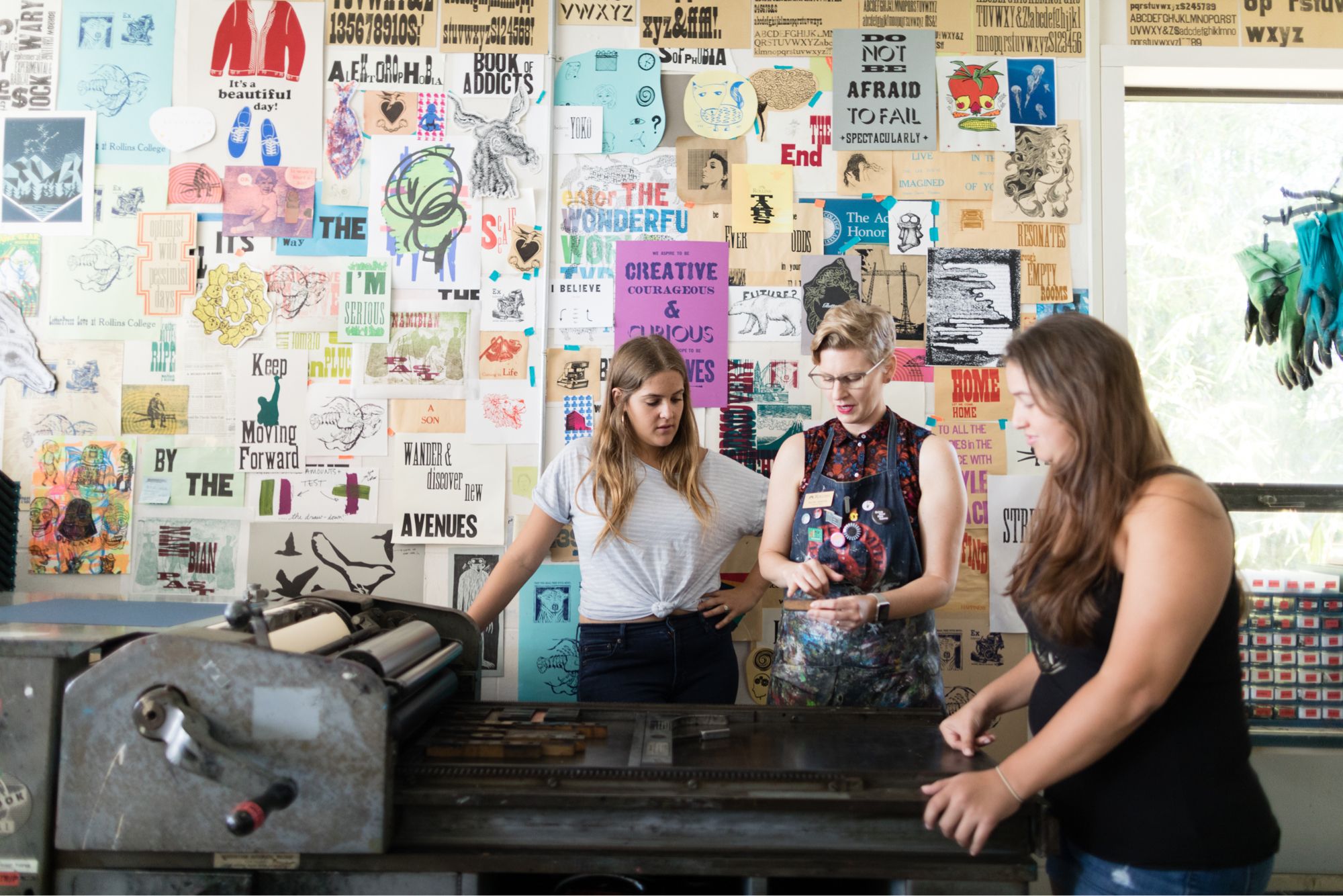 A professor shows two students how to use a vintage press.