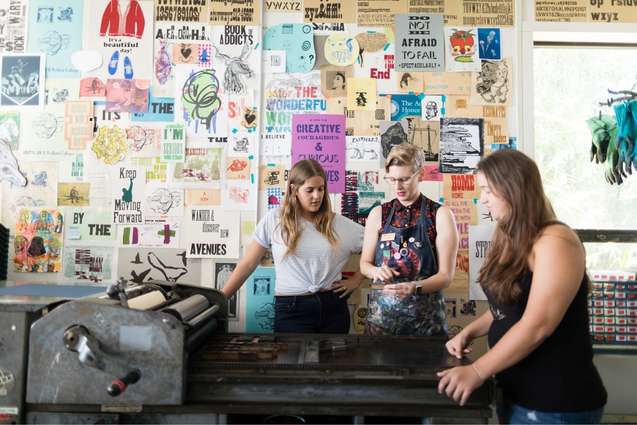 Art studio college students and mentor at a large screen printing press.