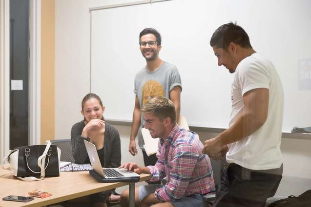 Students gathered around a friend on his computer laughing.