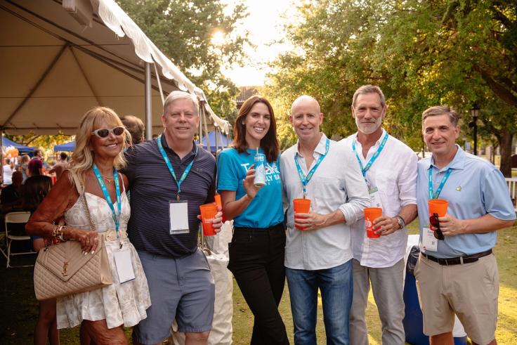 Group of adults smiling with drinks during Rollins Alumni Weekend’s Grove Party.