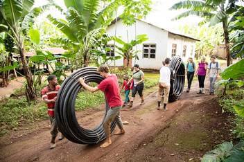 Students help local villagers carry building equipment in Tanzania.