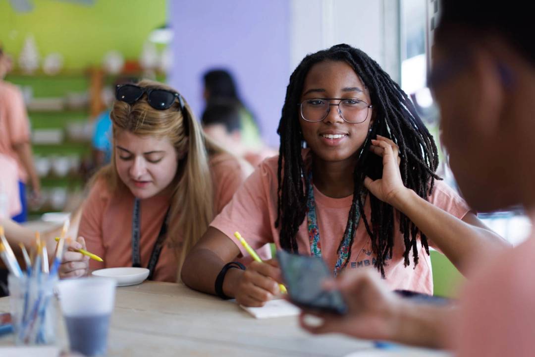 A student smiles at a classmate during a pottery course.