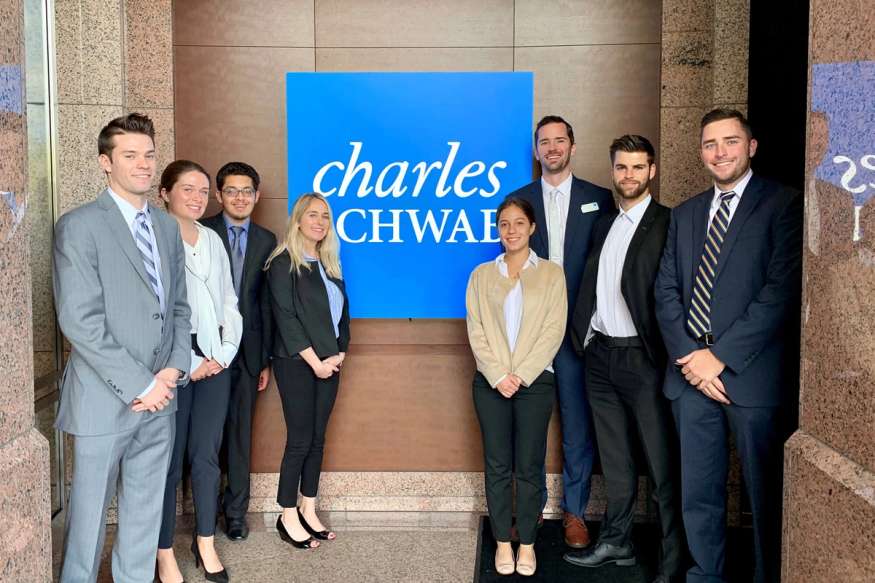 A group of college students pose in front of a Charles Schwab sign.