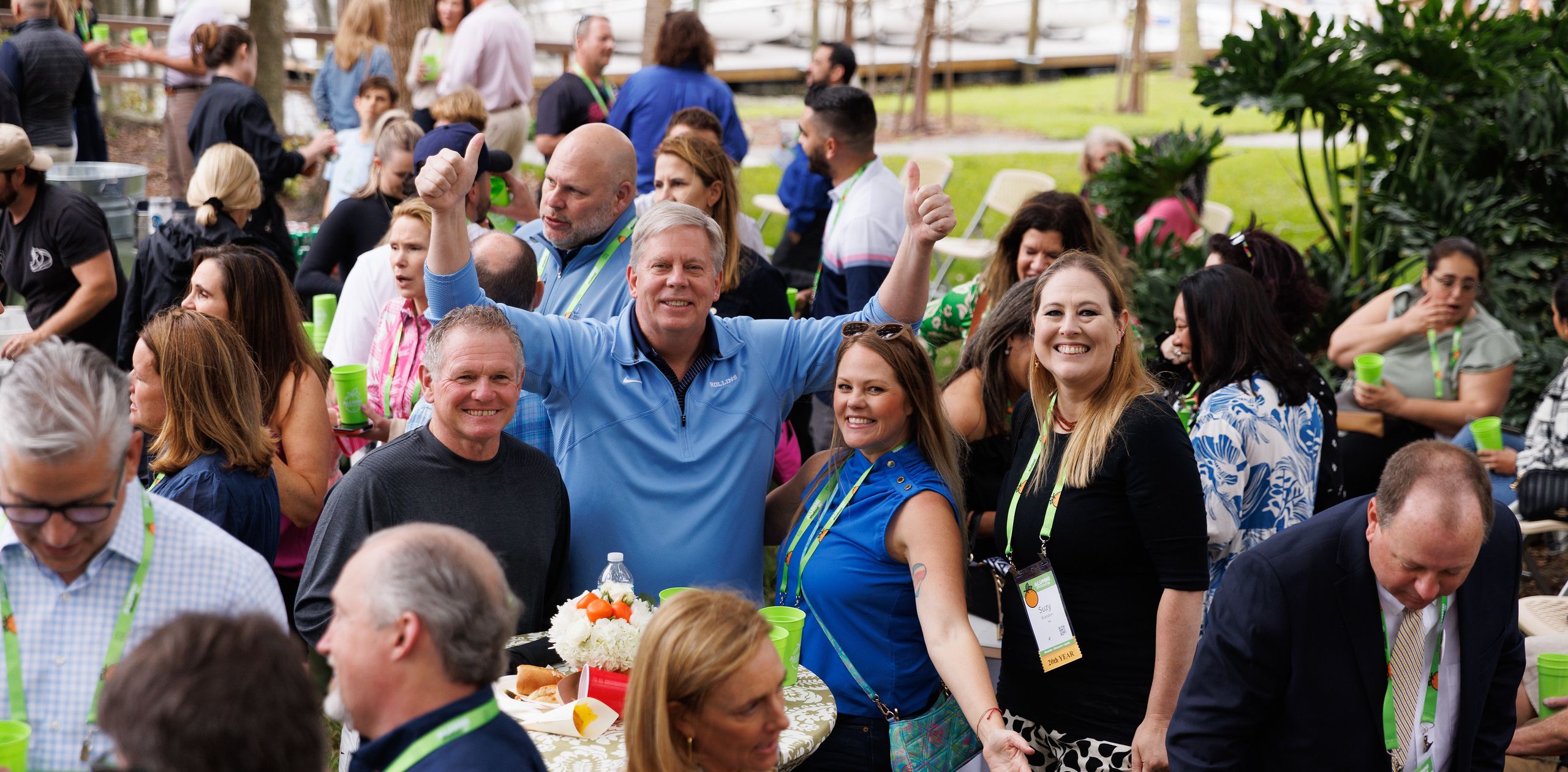 Crowd of alumni from Alumni Weekend, with four alumni in the center posing and one with two thumbs up.