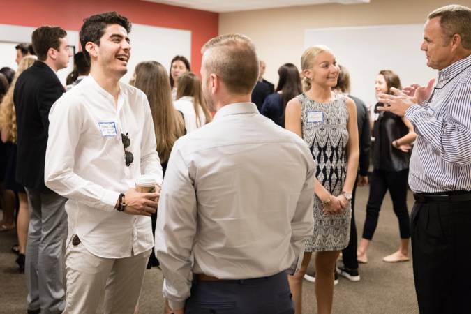 A group of college students dressed in business attire talking among themselves.