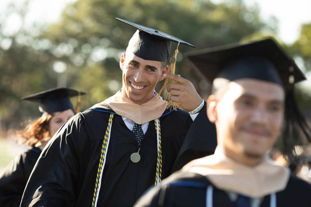 An adult college student smiles during a commencement ceremony.