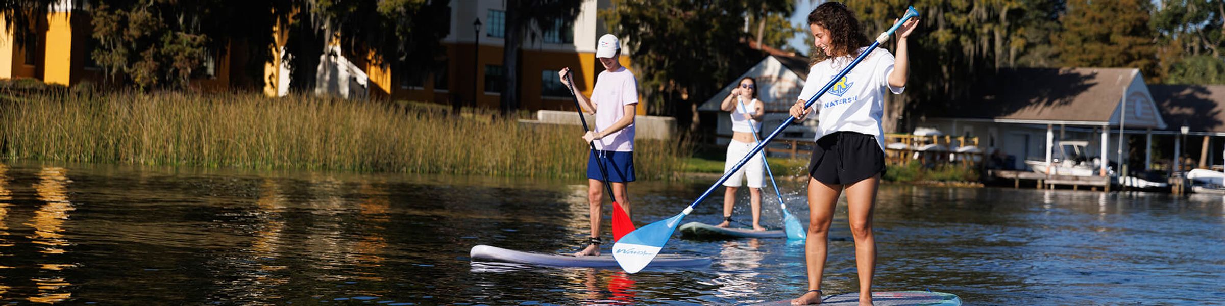 Three students paddle board on Lake Virginia near Rollins College.