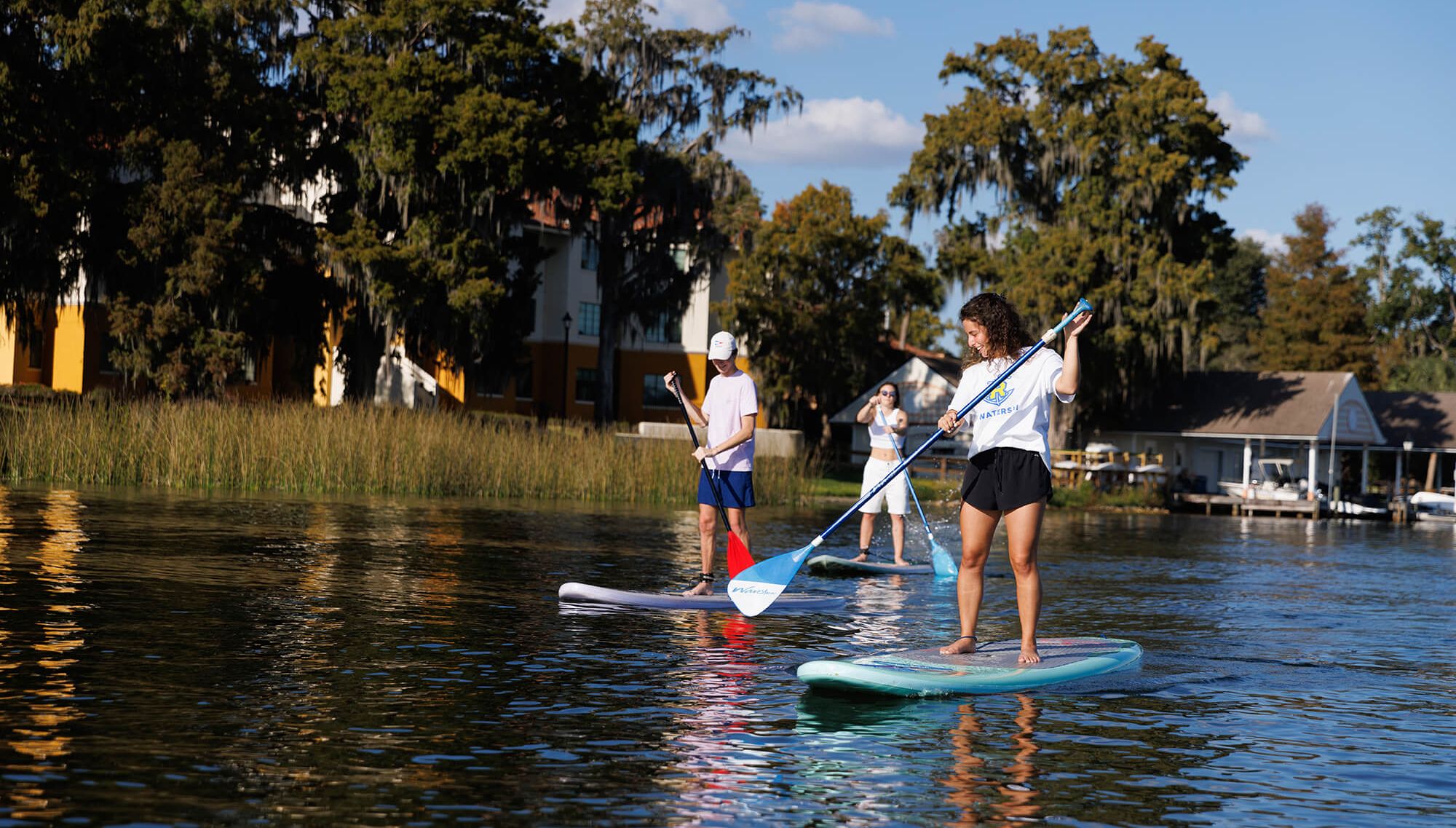Three students paddle board on Lake Virginia near Rollins College.