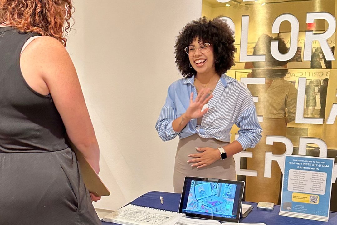 Woman smiles gesturing to lesson plans ona table in an art gallery