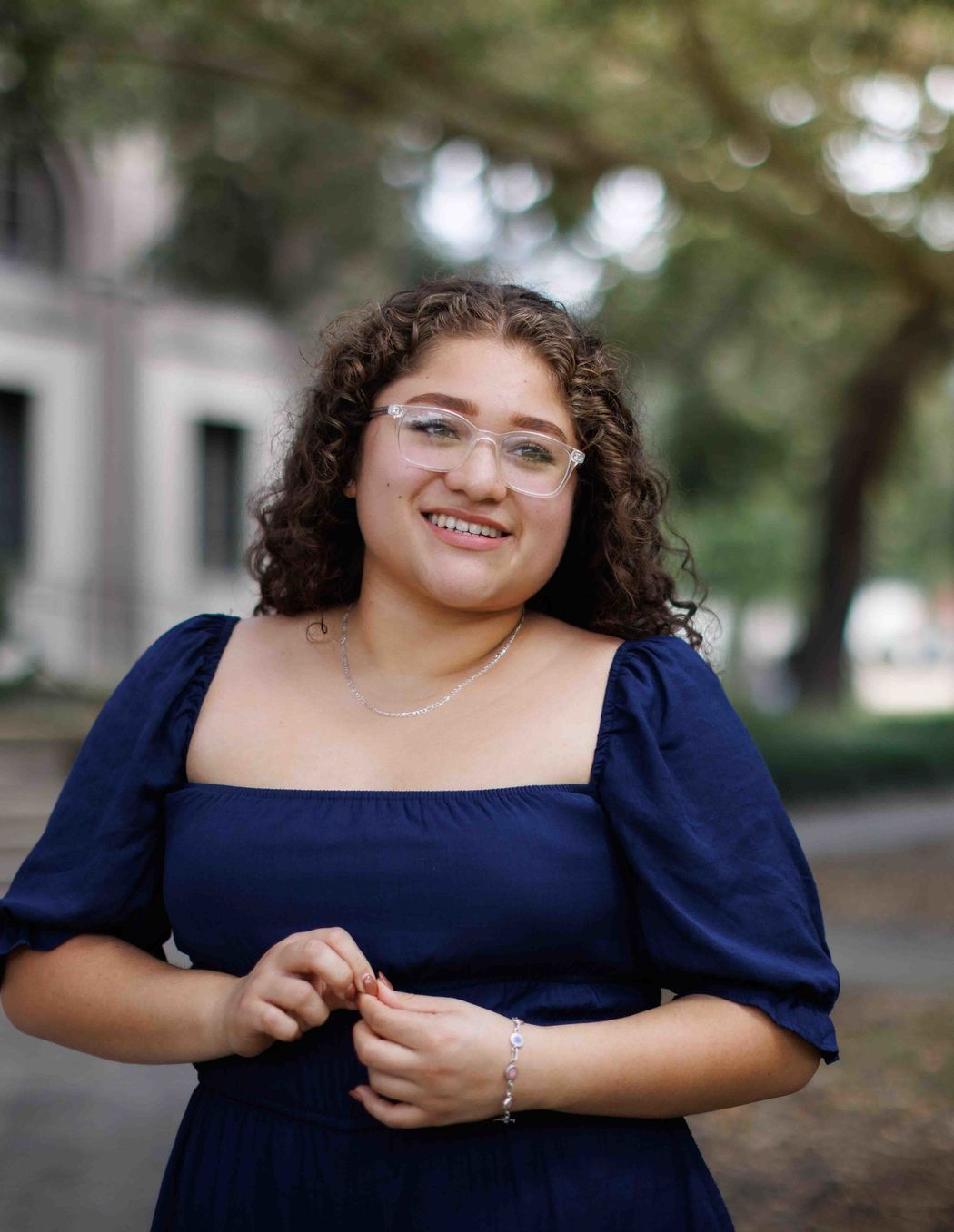 Michelle in a dark blue dress and clear-rimmed glasses smiling outside on Rollins campus.