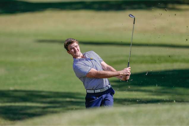 An athlete hitting a golf ball during a match.