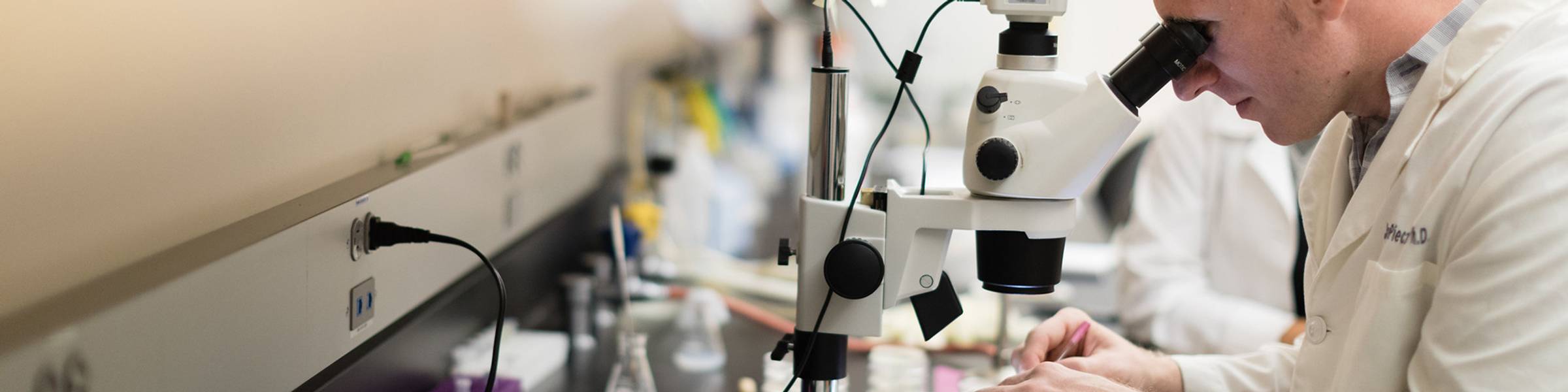 Rollins student looks into a microscope in a lab with many samples on the table