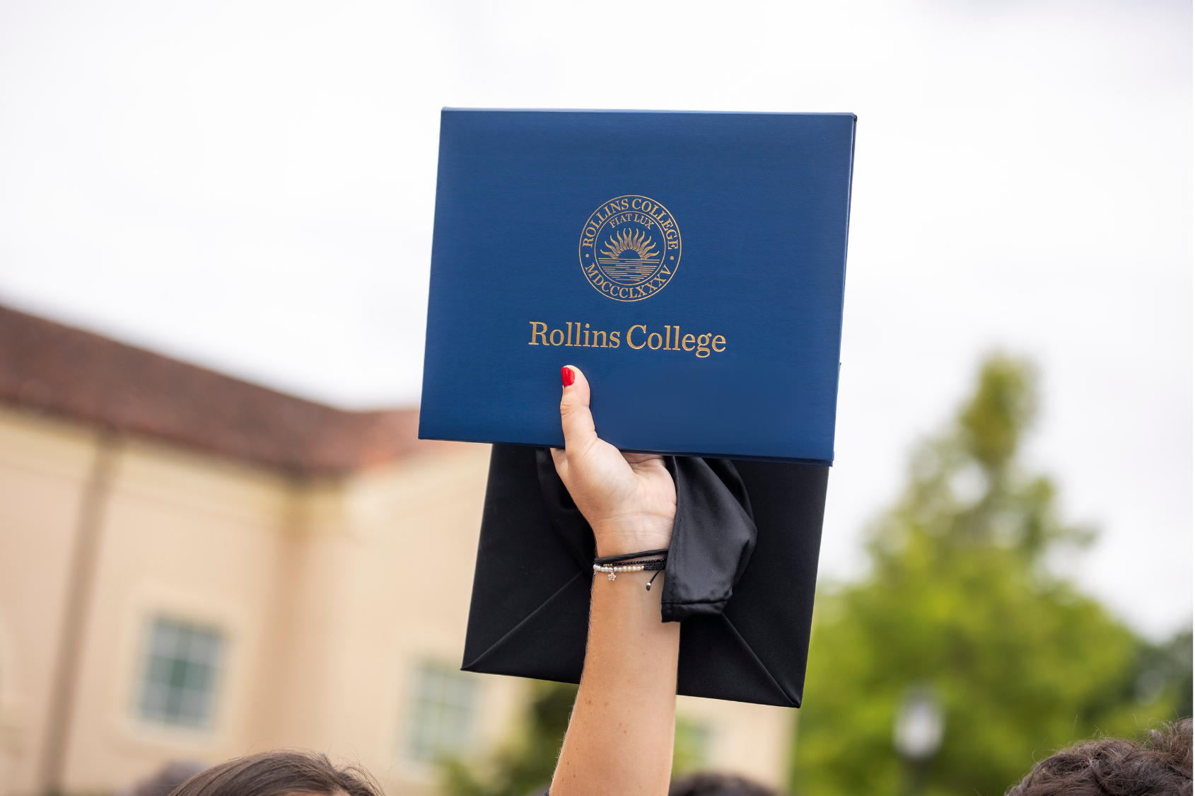 Hand holding a Rollins College diploma case in the air at graduation