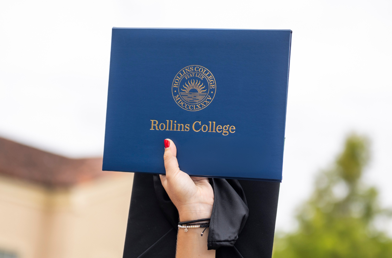 Hand holding a Rollins College diploma case in the air at graduation