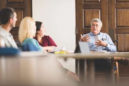 A humanities professor discusses a book with a group of students seated around a table.