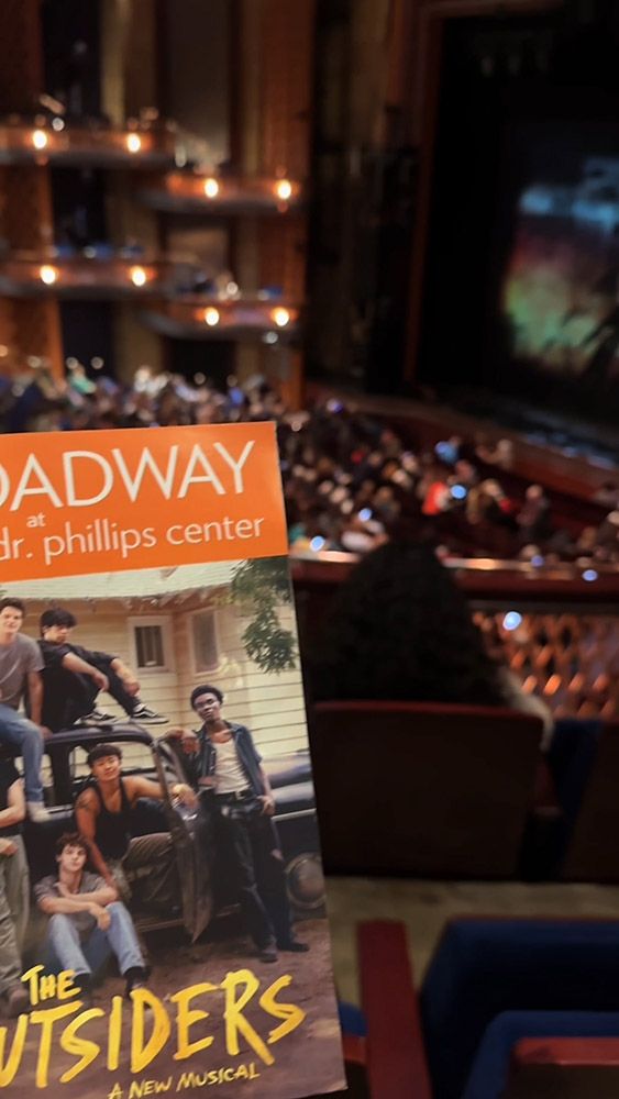 Playbill for The Outsiders musical held up inside theater auditorium.