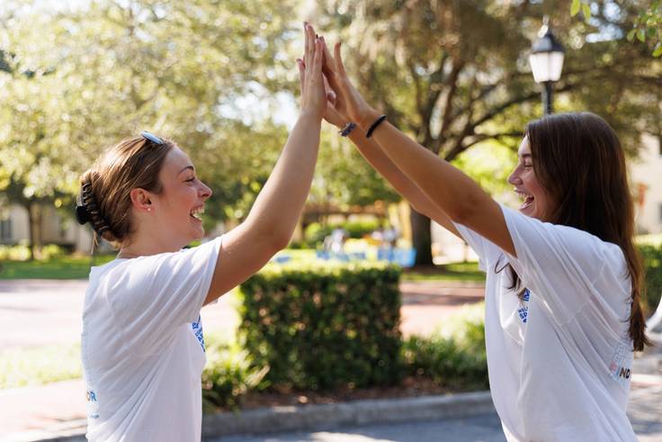 Two Rollins student high five on campus. 