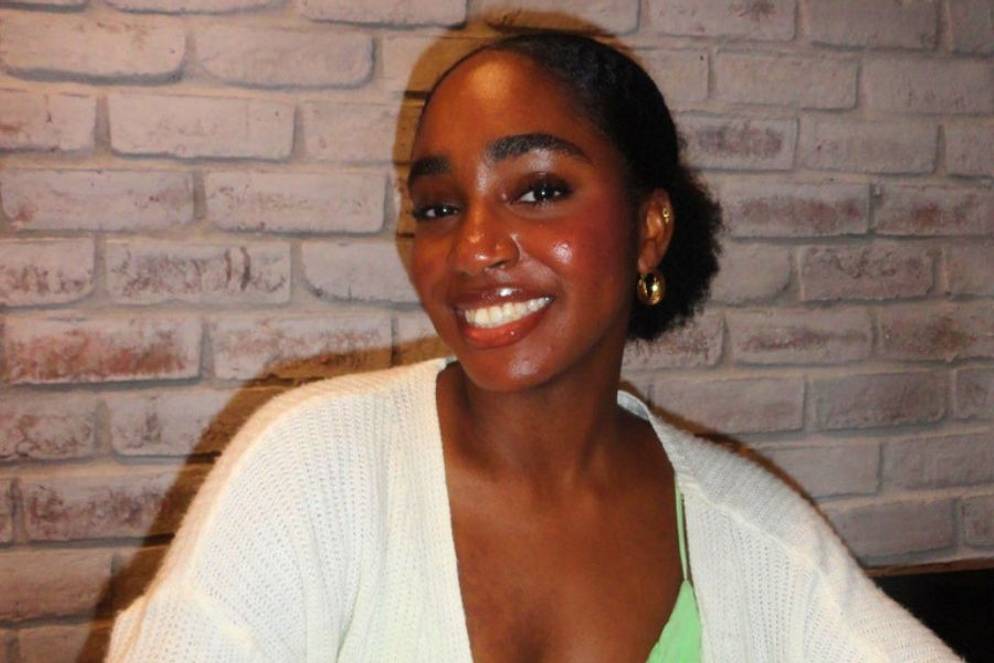 Smiling Marcelle Romulus ’27 in cozy sweater posing against a light brick wall.