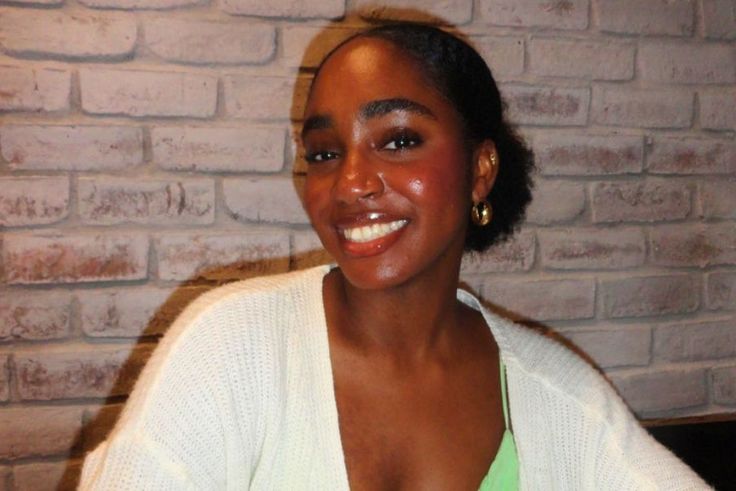 Smiling Marcelle Romulus ’27 in cozy sweater posing against a light brick wall.