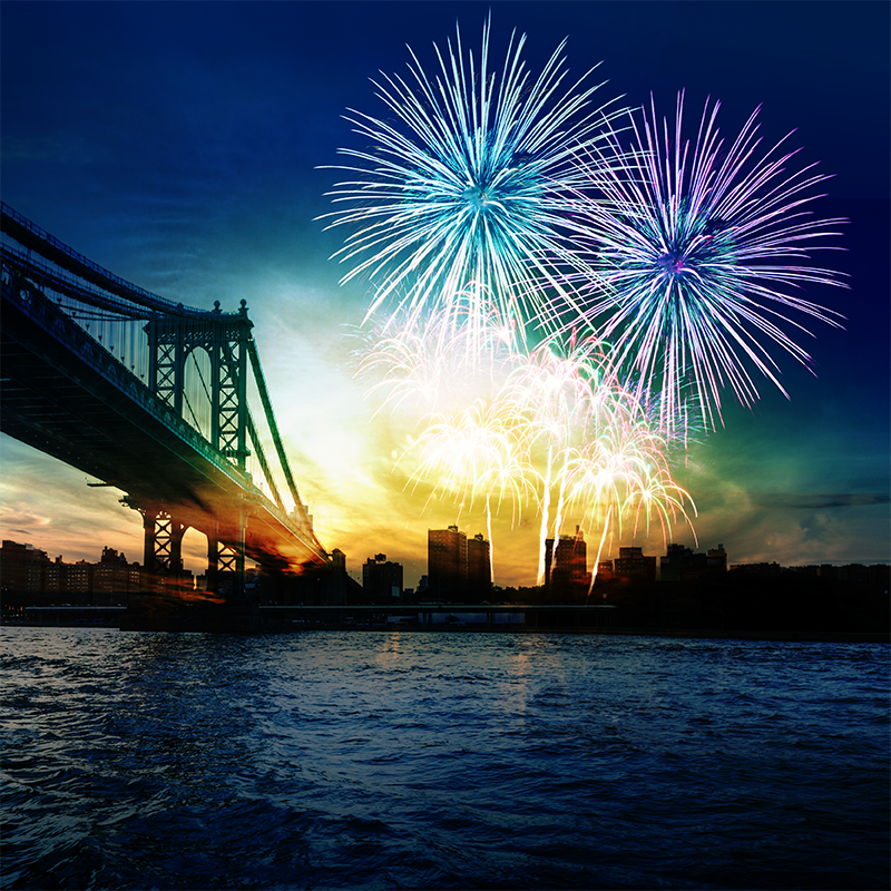 Colorful fireworks over city skyline and bridge reflecting on water