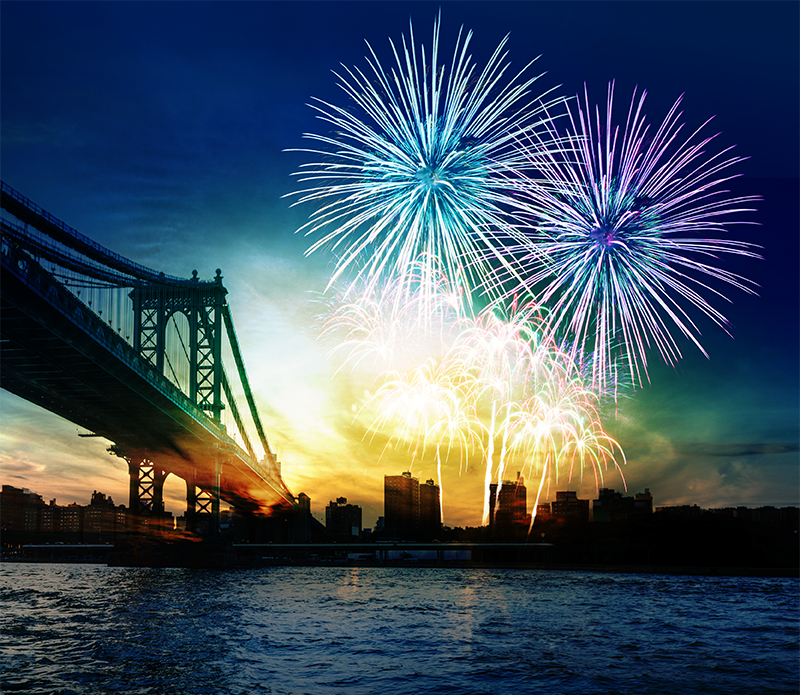 Colorful fireworks over city skyline and bridge reflecting on water