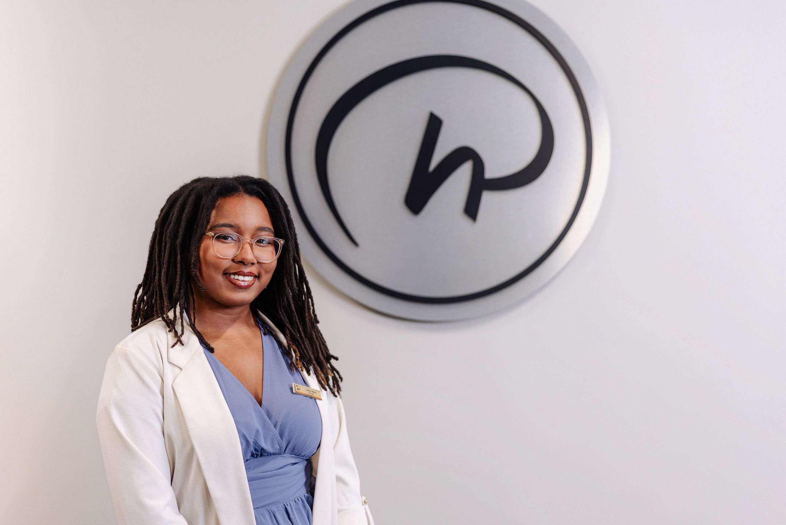 Smiling student in a white blazer and blue dress stands beside the Rosen Hotels & Resorts logo mounted on a wall.