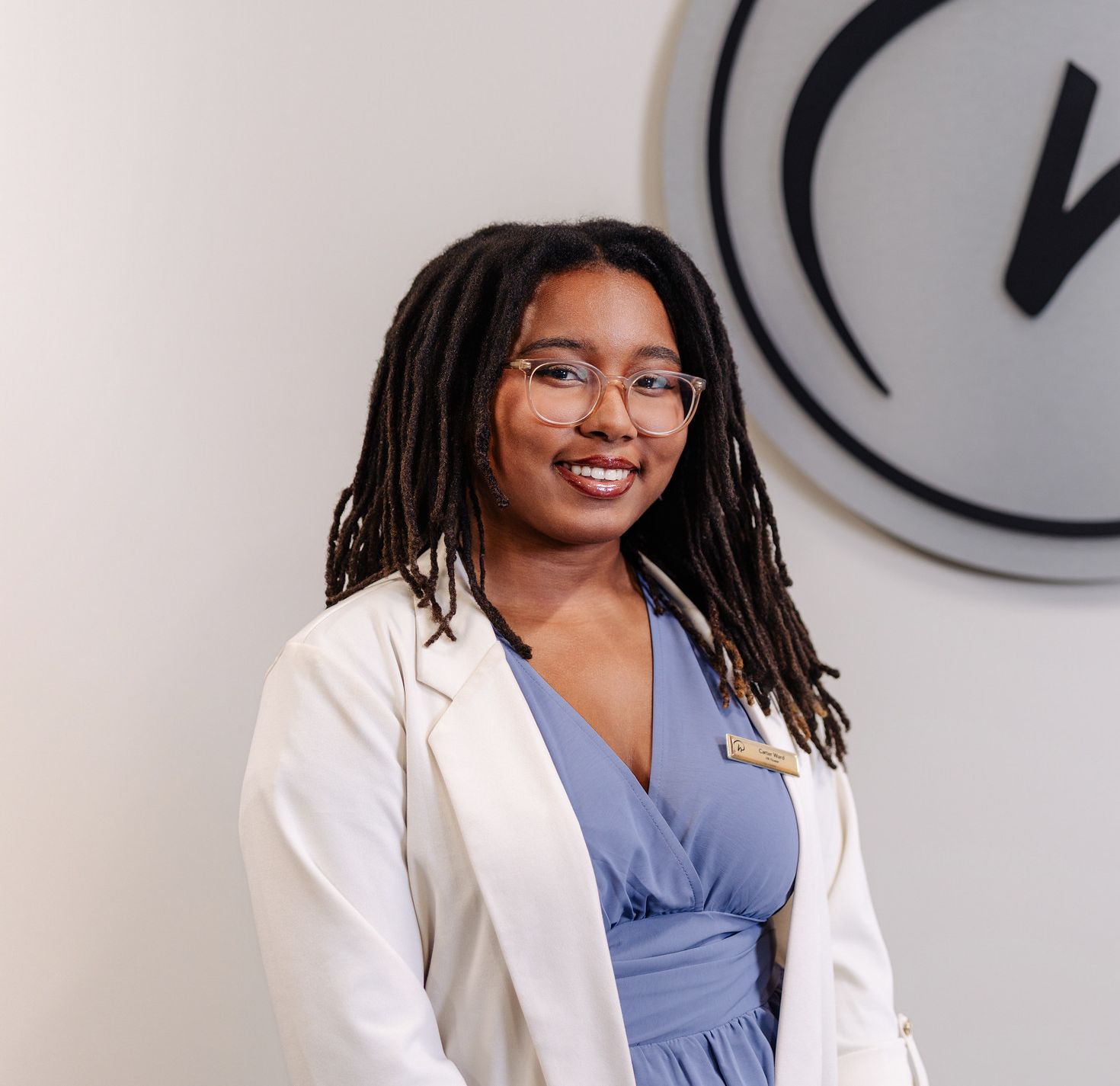 Smiling student in a white blazer and blue dress stands beside the Rosen Hotels & Resorts logo mounted on a wall.