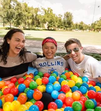 A group of Rollins student laugh while in. a ball pit at a on campus event. 