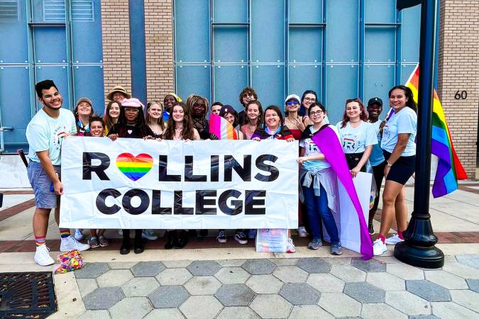 Members of Spectrum pose outside in downtown Orlando holding a Rollins College rainbow pride banner.