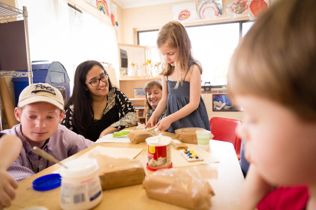 Children sit around a table with a philosophy student, working on their artwork.