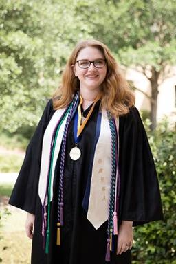 A college graduate poses on campus in her cap and gown.
