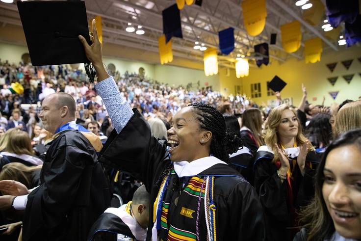 Rollins student holding up diploma on graduation day.