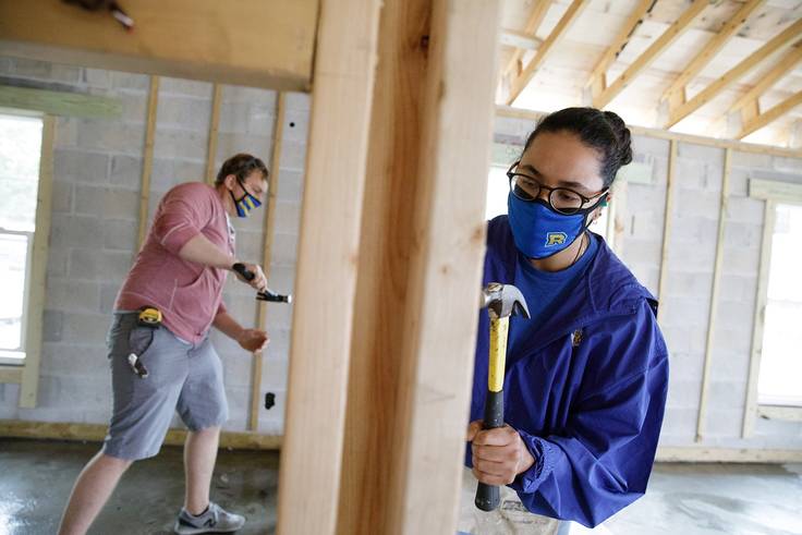Two college students work on a Habitat for Humanity house build.