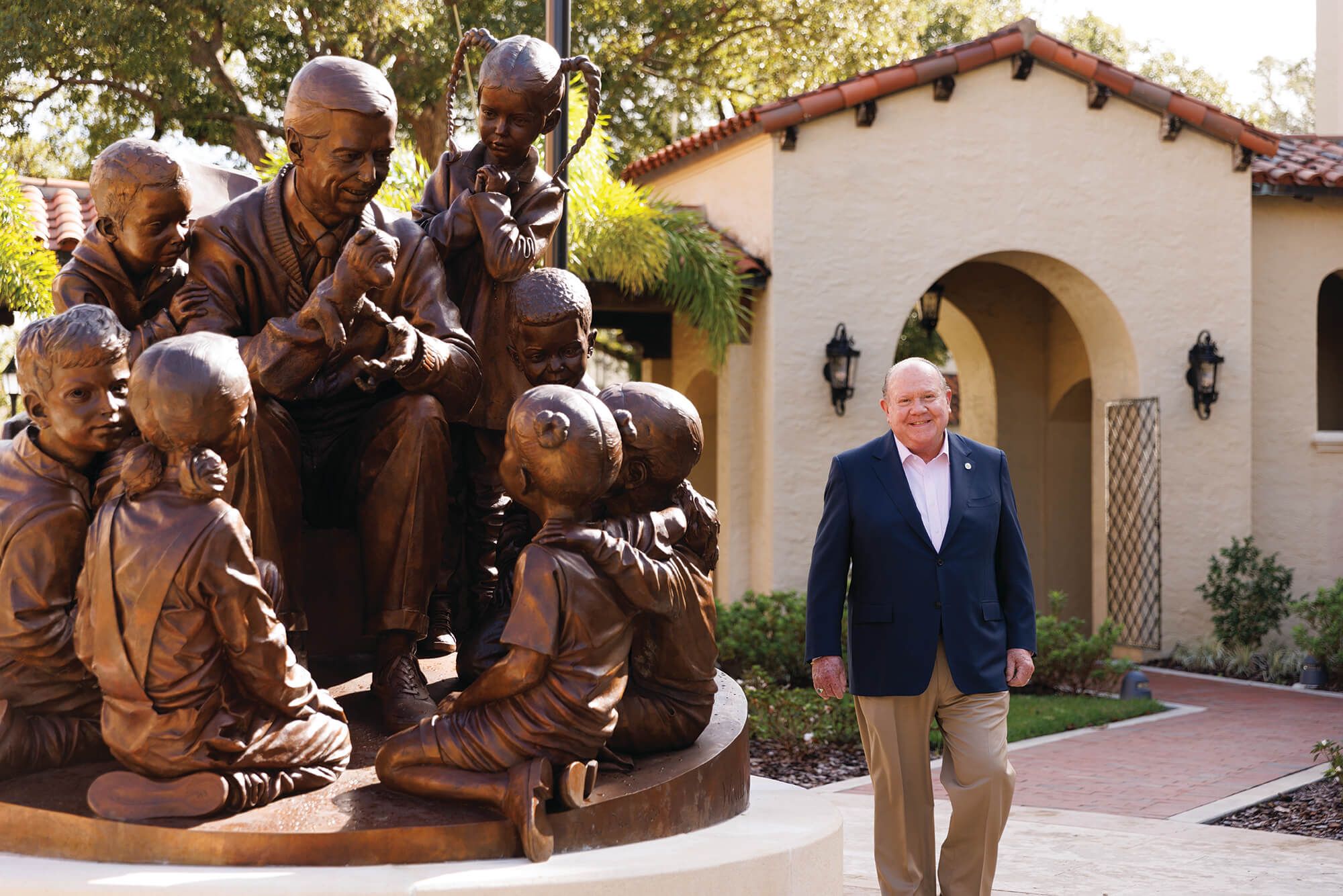 Allan E. Keen ’70 ’71MBA ’10H stands beside bronze sculpture of educator surrounded by children.