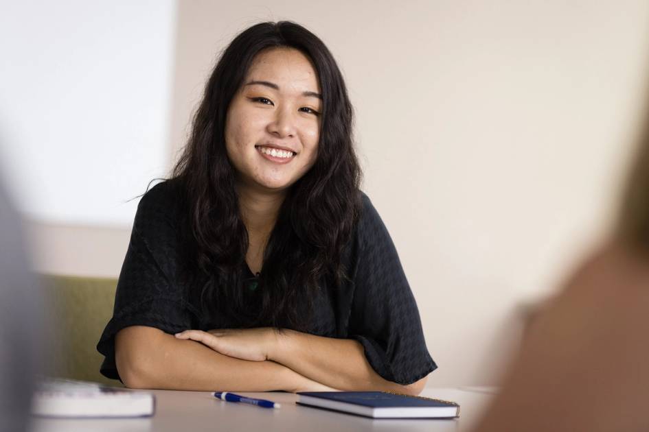 A college student smiles at the camera during class.