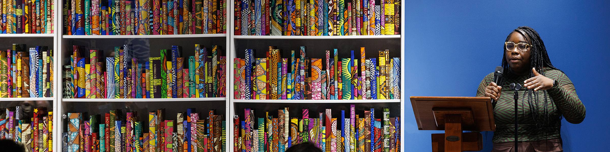 A student stands at a podium and delivers a talk about an art installation.