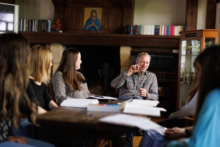 A humanities professor explains a concept to a small group of students seated around a table.