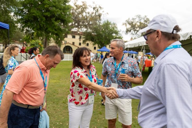 Rollins alumni shaking hands jovially on Mills Lawn.