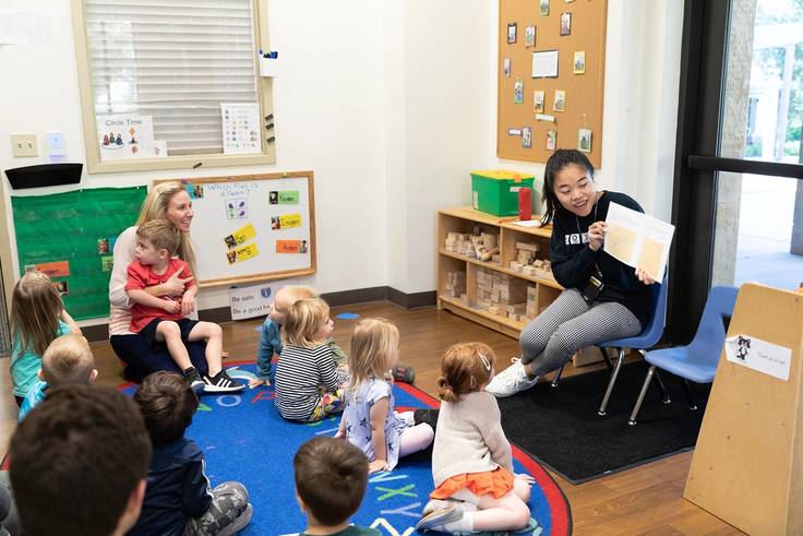 A college student reading to a class of children at the children's development center (CDC).