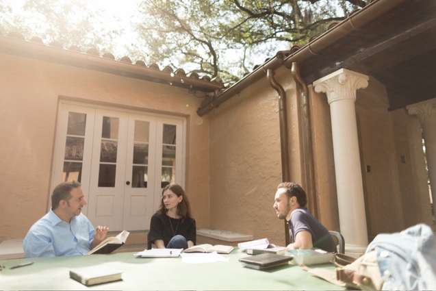 Religious studies college students talking with their professor outside at the table of the outdoor classroom.