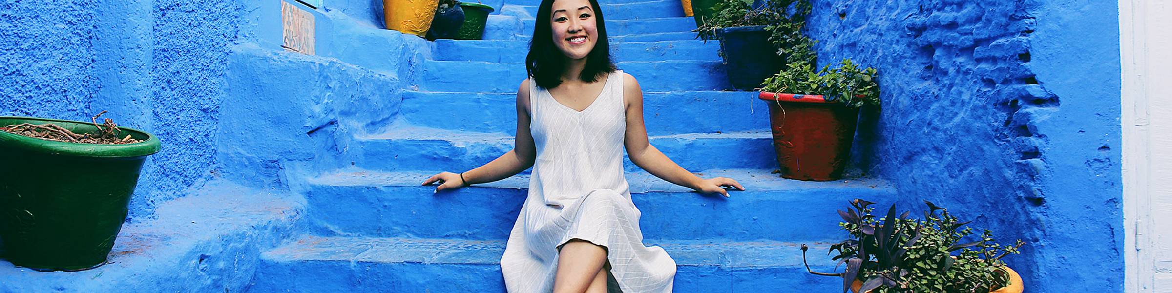 A college student poses for a photo on a blue staircase in Morocco.