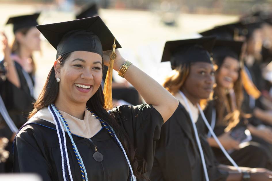 A adult college graduate smiles during a commencement ceremony.