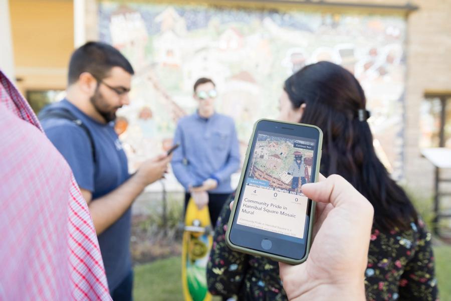 Group of students standing in front of a wall mural. Smartphone with photo of the mural.