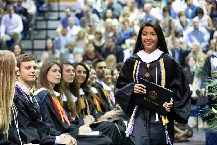 A Rollins student smiles as she walks with her diploma in her hands.