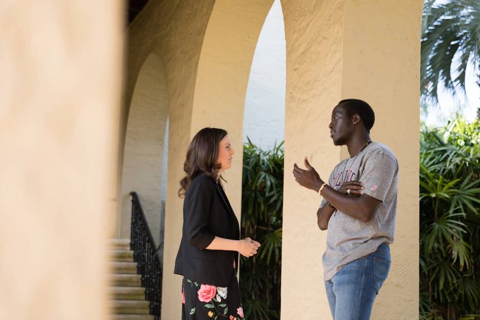 Rollins alumni and student having a conversation in a hallway.